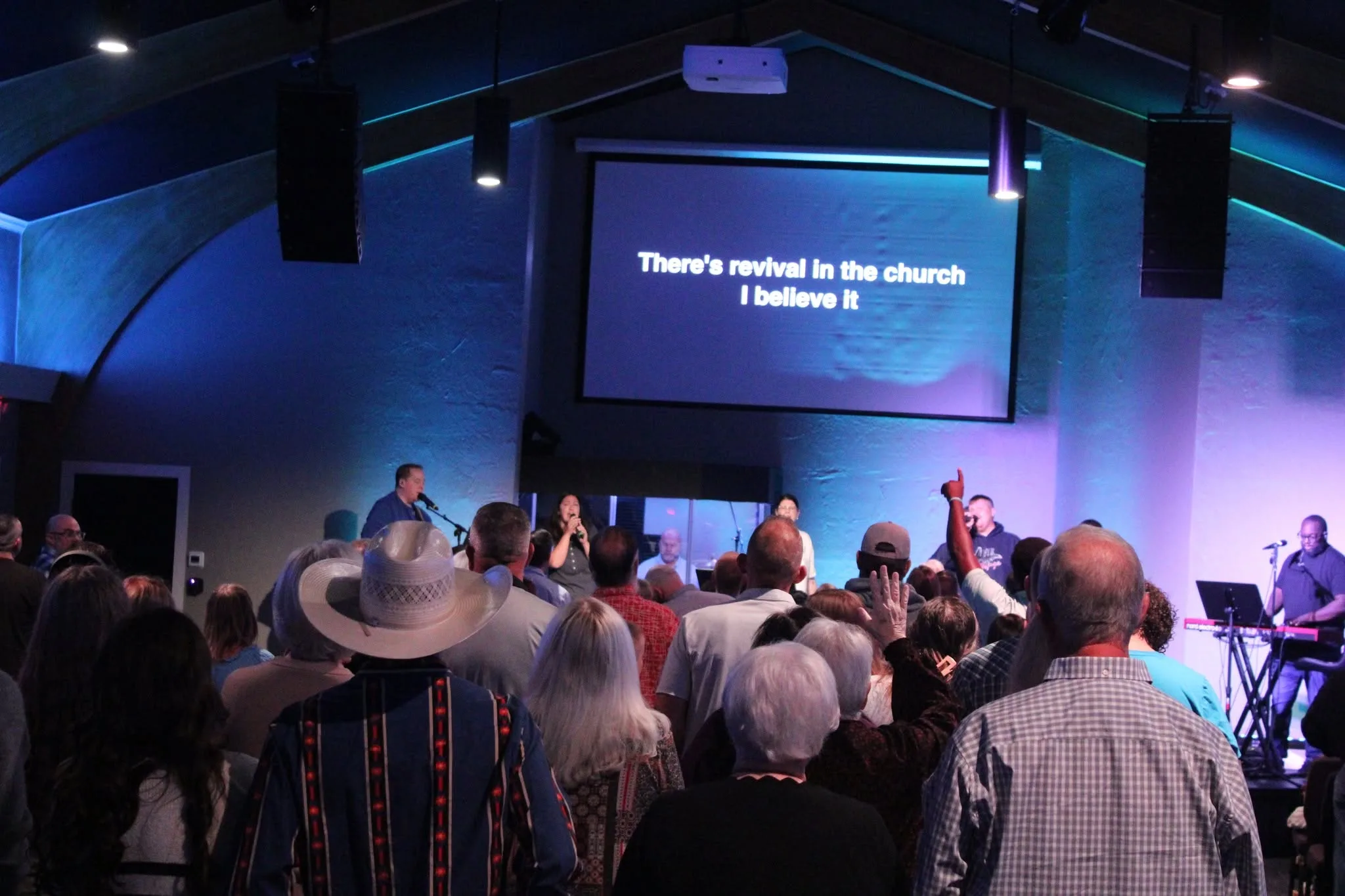 People gathered in the sanctuary with hands raised during a Refuge service.