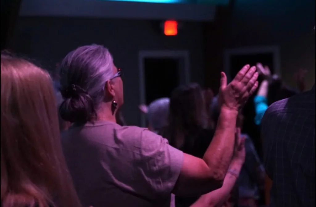 A woman with her hand raised in worship among the congregation at The Refuge.