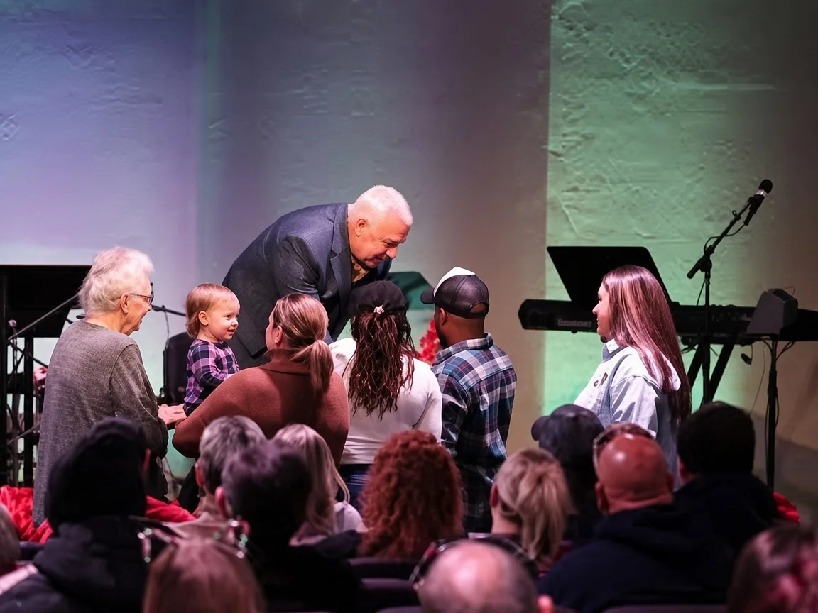 A pastor leaning down to greet a toddler and family during a gathering at The Refuge.